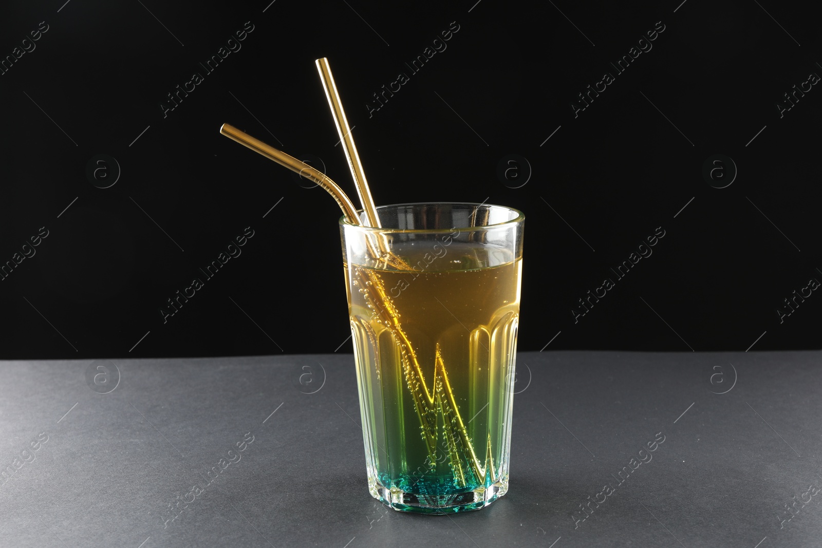 Photo of Tasty refreshing drink with straws in glass on grey table