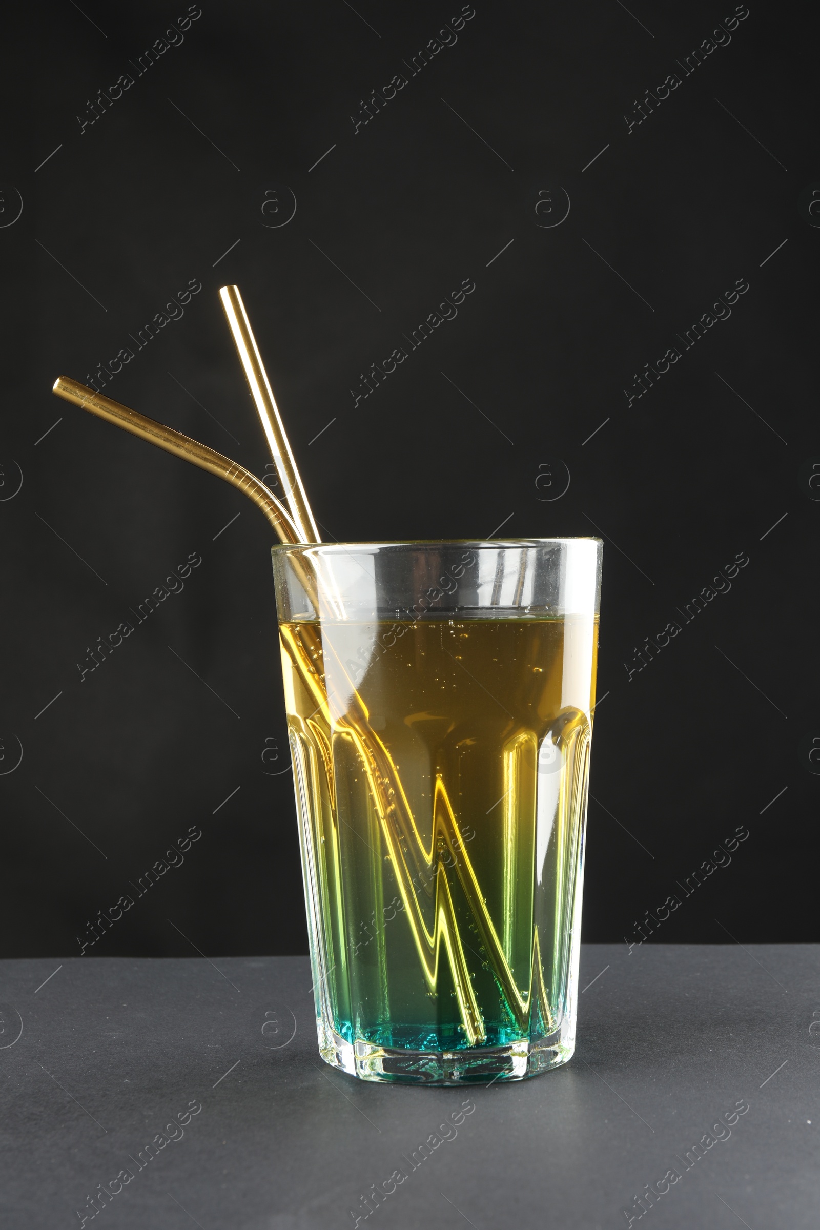 Photo of Tasty refreshing drink with straws in glass on grey table