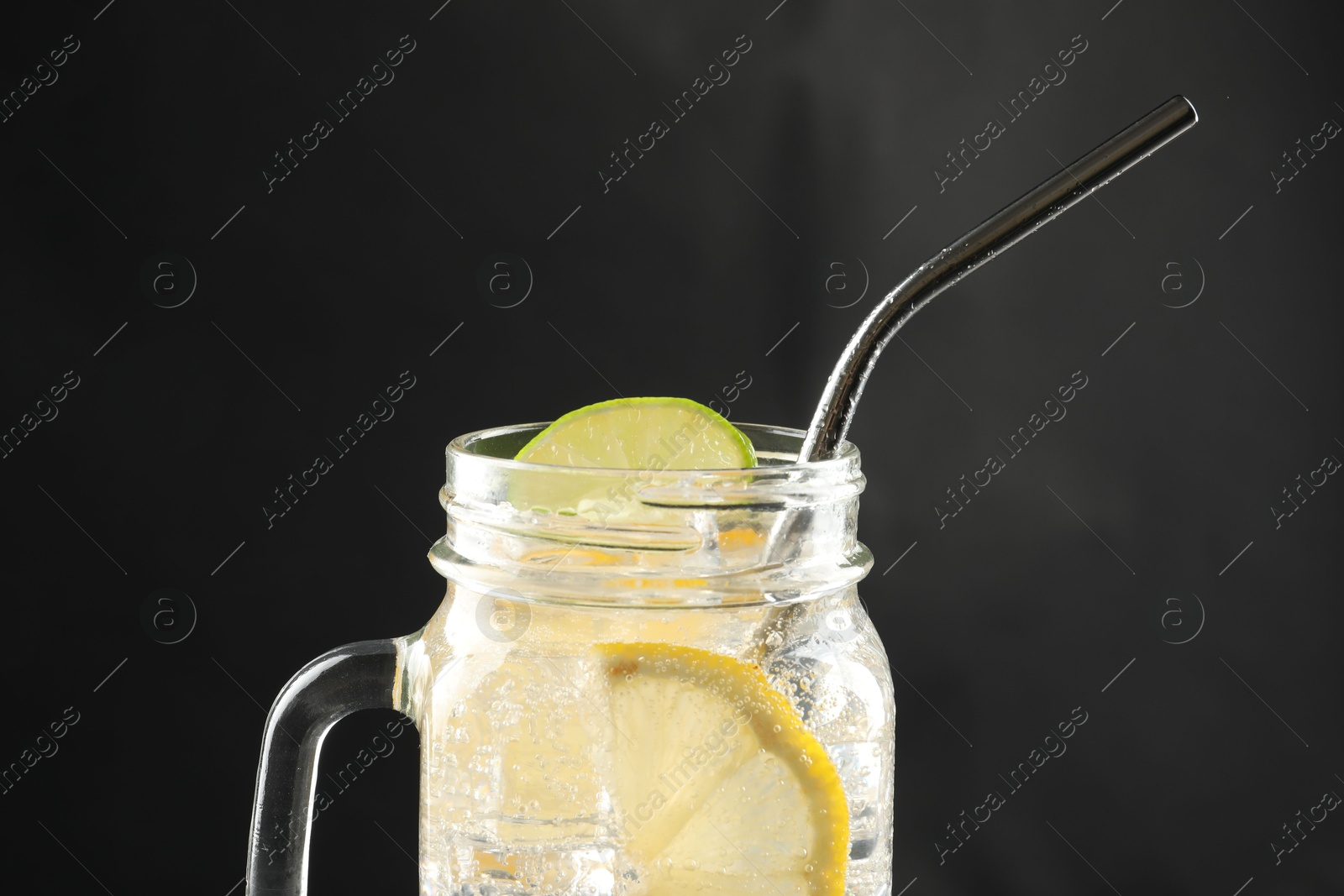 Photo of Tasty refreshing drink with straw in mason jar on dark background, closeup