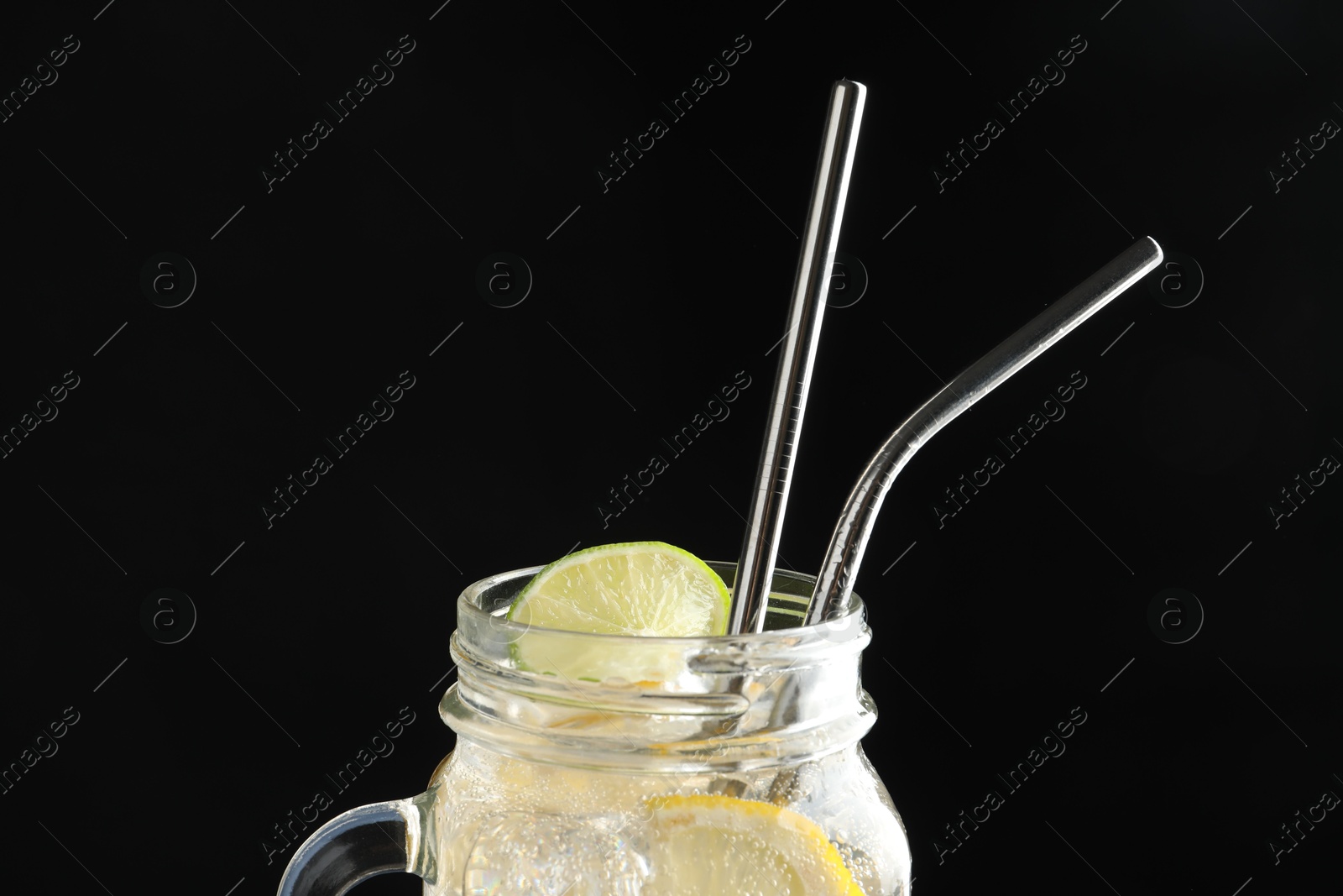 Photo of Tasty refreshing drink with straws in mason jar on dark background, closeup