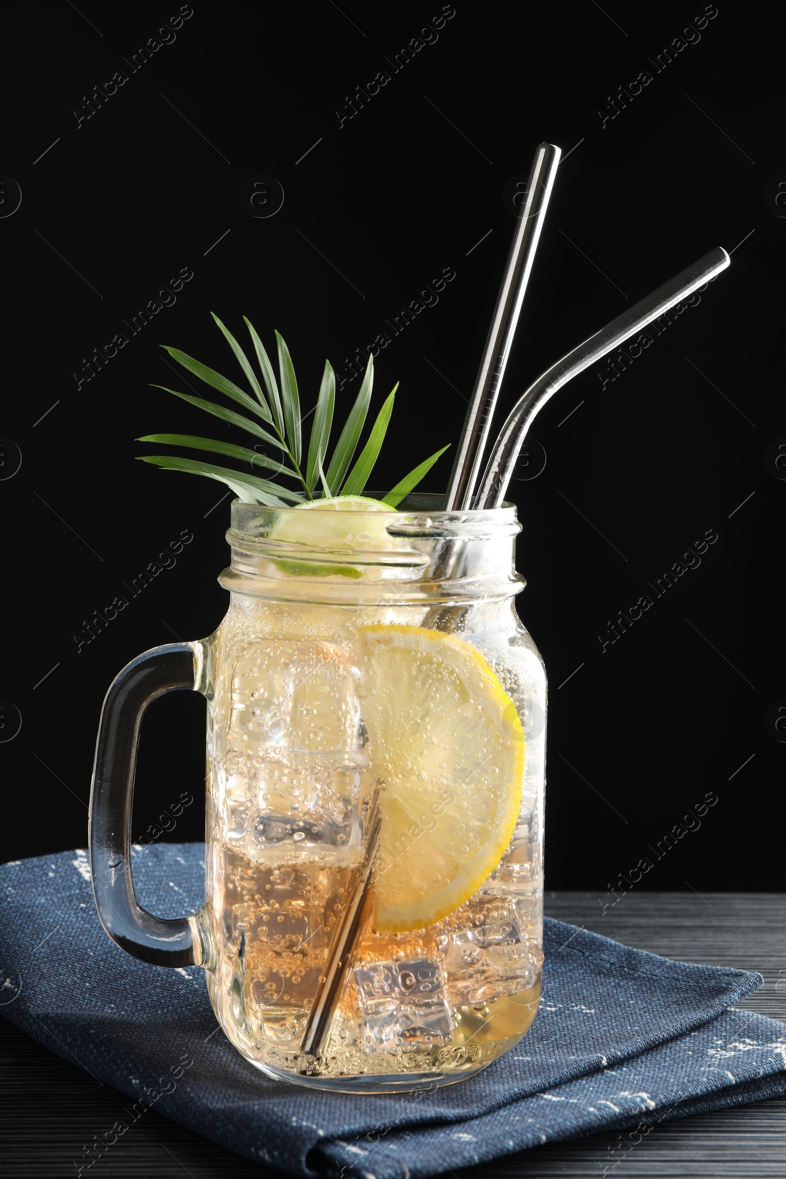 Photo of Tasty refreshing drink with straws in mason jar on black wooden table