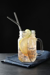 Tasty refreshing drink with straws in mason jar on black wooden table