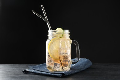 Photo of Tasty refreshing drink with straws in mason jar on black wooden table