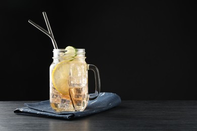 Tasty refreshing drink with straws in mason jar on black wooden table, space for text