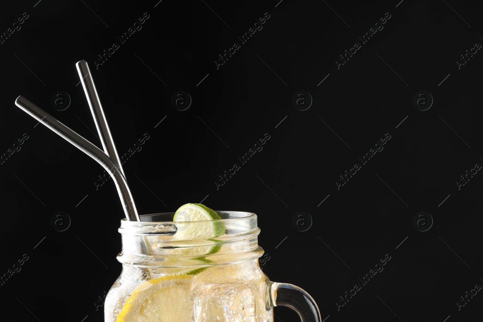 Photo of Tasty refreshing drink with straws in mason jar on black background, space for text