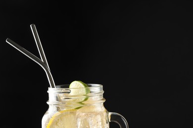 Photo of Tasty refreshing drink with straws in mason jar on black background, space for text