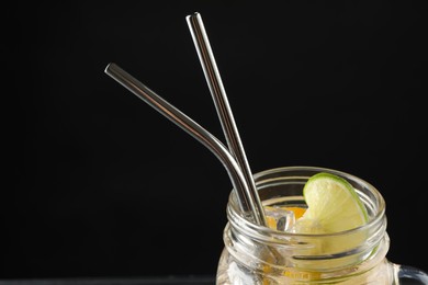 Photo of Tasty refreshing drink with straws in mason jar on black background, closeup