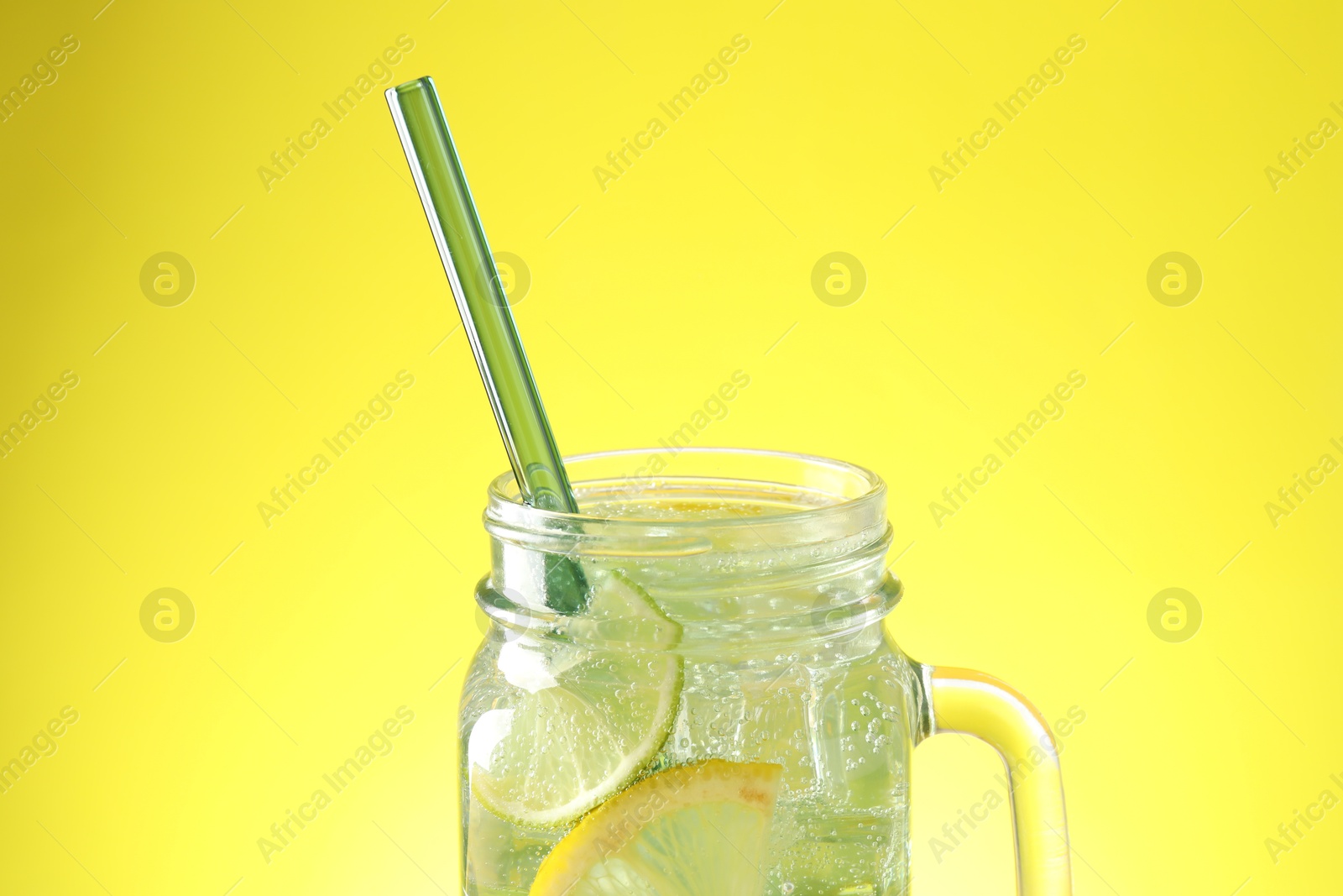 Photo of Tasty refreshing drink with straw in mason jar on yellow background, closeup