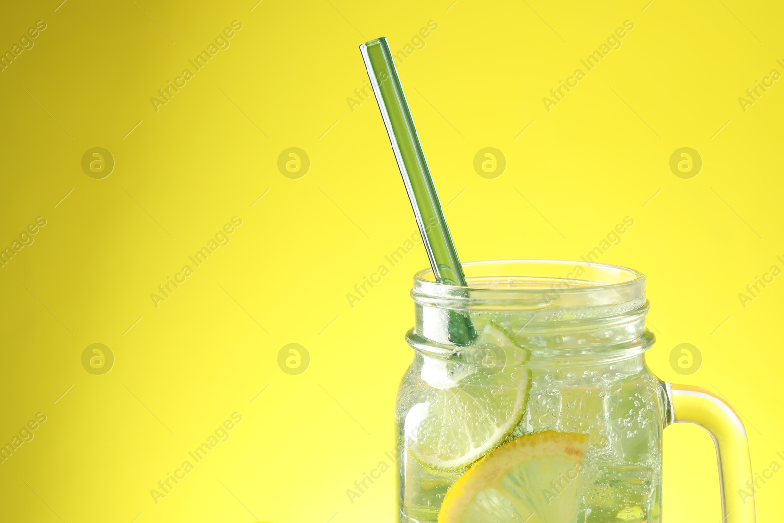 Photo of Tasty refreshing drink with straw in mason jar on yellow background, closeup. Space for text