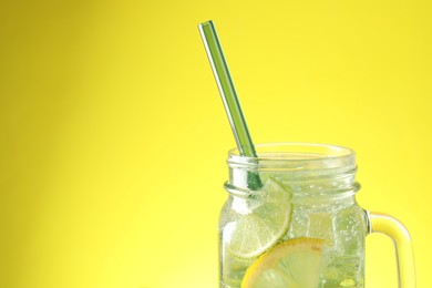 Photo of Tasty refreshing drink with straw in mason jar on yellow background, closeup. Space for text