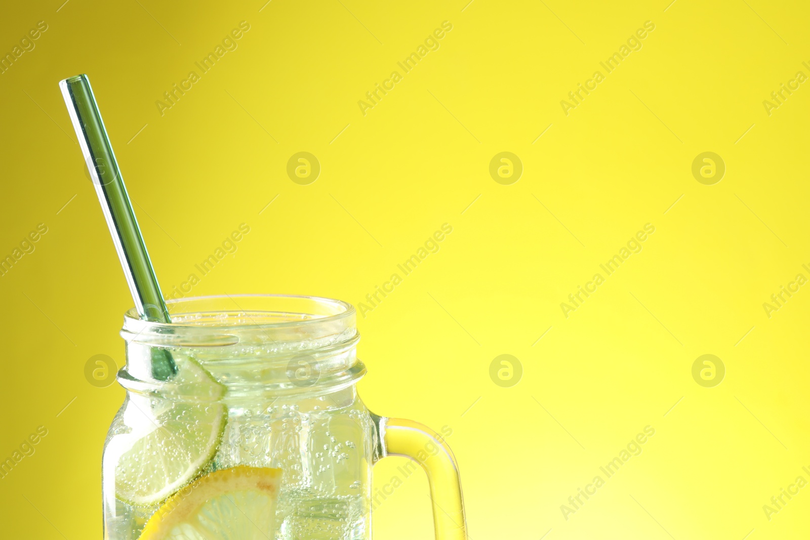 Photo of Tasty refreshing drink with straw in mason jar on yellow background, closeup. Space for text