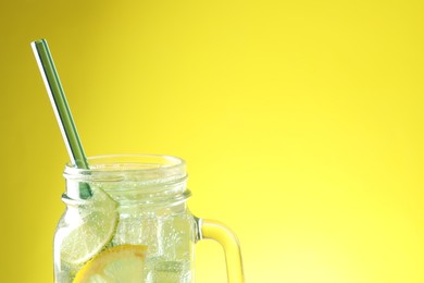 Photo of Tasty refreshing drink with straw in mason jar on yellow background, closeup. Space for text