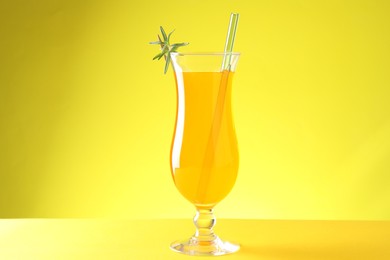 Tasty refreshing drink with straw in glass on yellow background