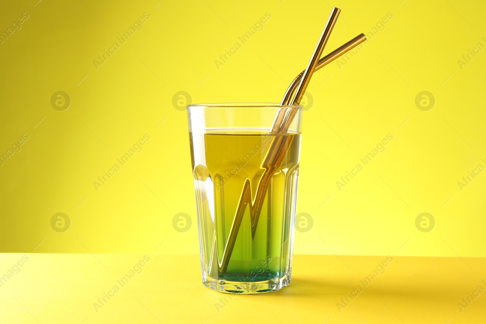 Photo of Tasty refreshing drink with straws in glass on yellow background