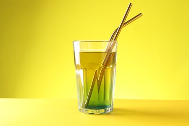 Photo of Tasty refreshing drink with straws in glass on yellow background