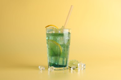 Photo of Tasty refreshing drink with straw in glass, lime and ice cubes on beige background