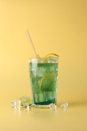 Tasty refreshing drink with straw in glass, lime and ice cubes on beige background