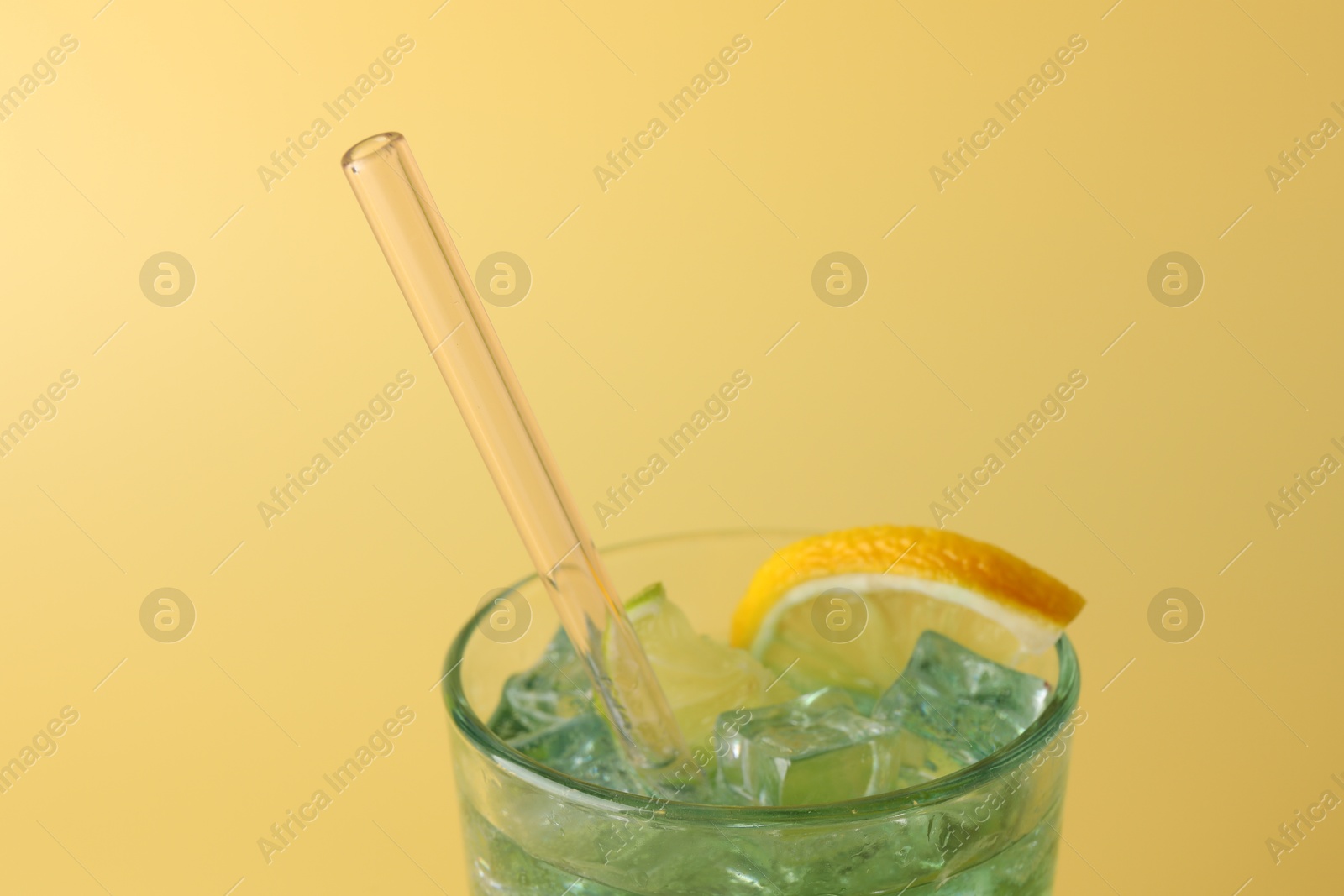 Photo of Tasty refreshing drink with straw in glass on beige background, closeup