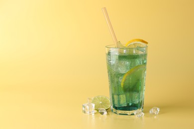 Tasty refreshing drink with straw in glass, lime and ice cubes on beige background, space for text