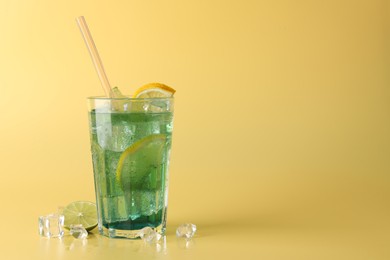 Photo of Tasty refreshing drink with straw in glass, lime and ice cubes on beige background, space for text