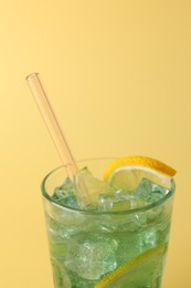 Photo of Tasty refreshing drink with straw in glass on beige background, closeup