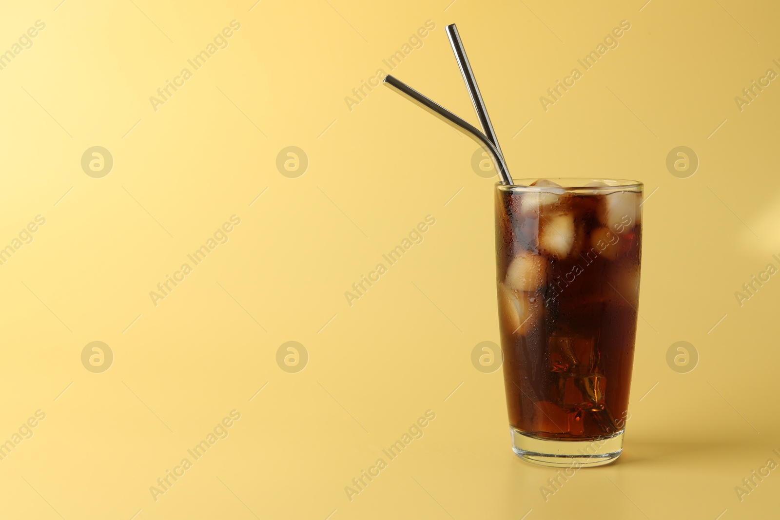 Photo of Tasty refreshing drink with straws in glass on beige background, space for text