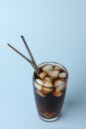 Photo of Tasty refreshing drink with straws in glass on light blue background