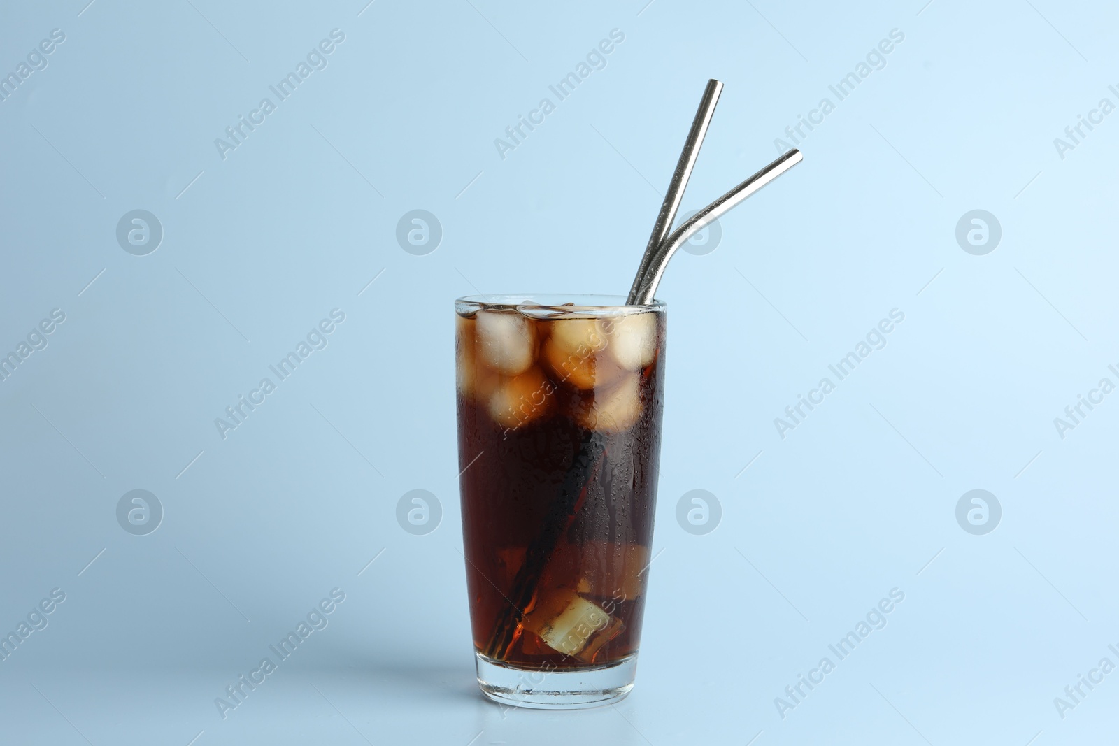 Photo of Tasty refreshing drink with straws in glass on light blue background