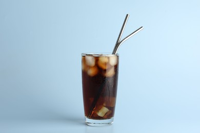 Photo of Tasty refreshing drink with straws in glass on light blue background