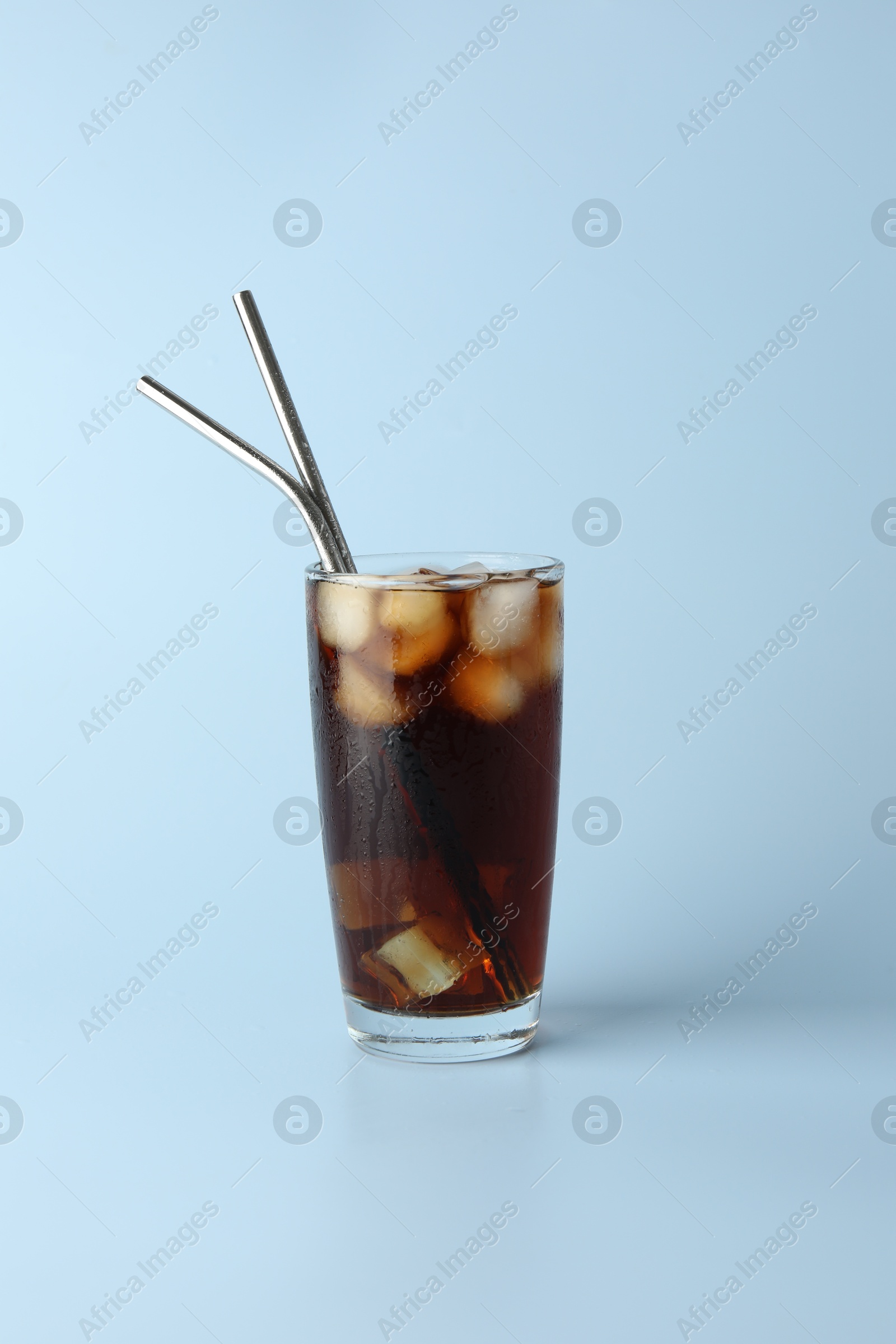 Photo of Tasty refreshing drink with straws in glass on light blue background