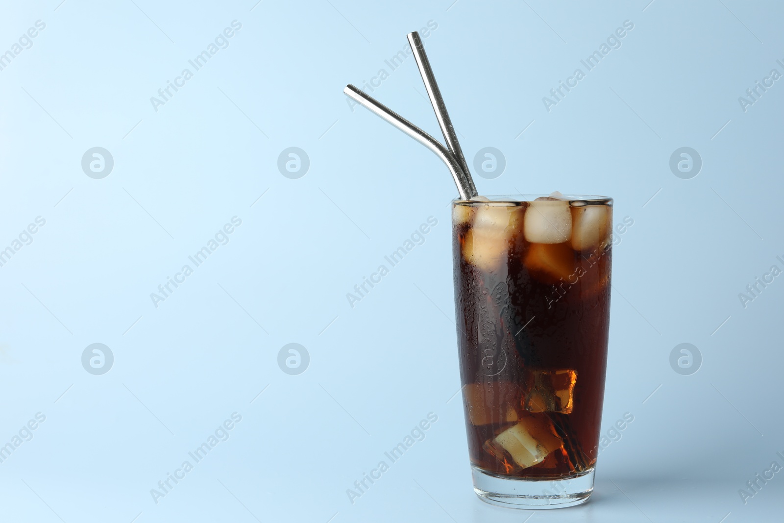 Photo of Tasty refreshing drink with straws in glass on light blue background, space for text