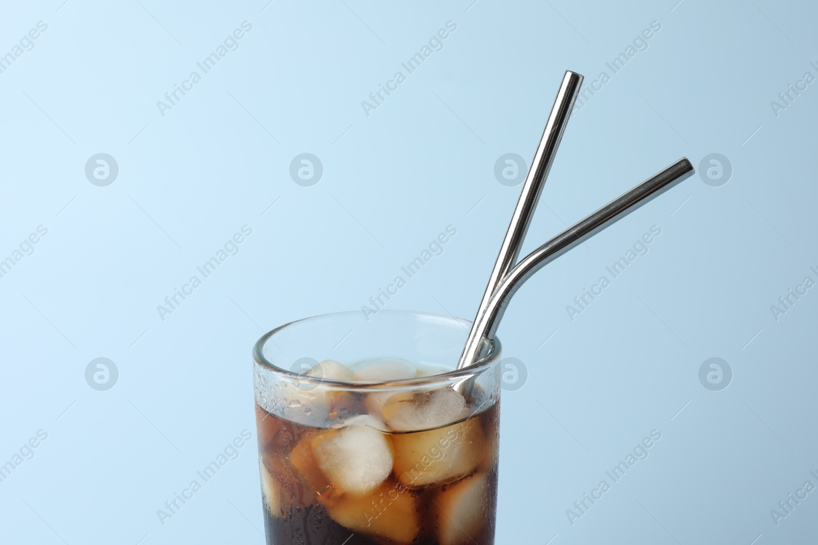 Photo of Tasty refreshing drink with straws in glass on light blue background, closeup