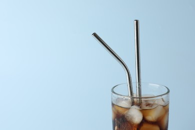 Tasty refreshing drink with straws in glass on light blue background, closeup. Space for text