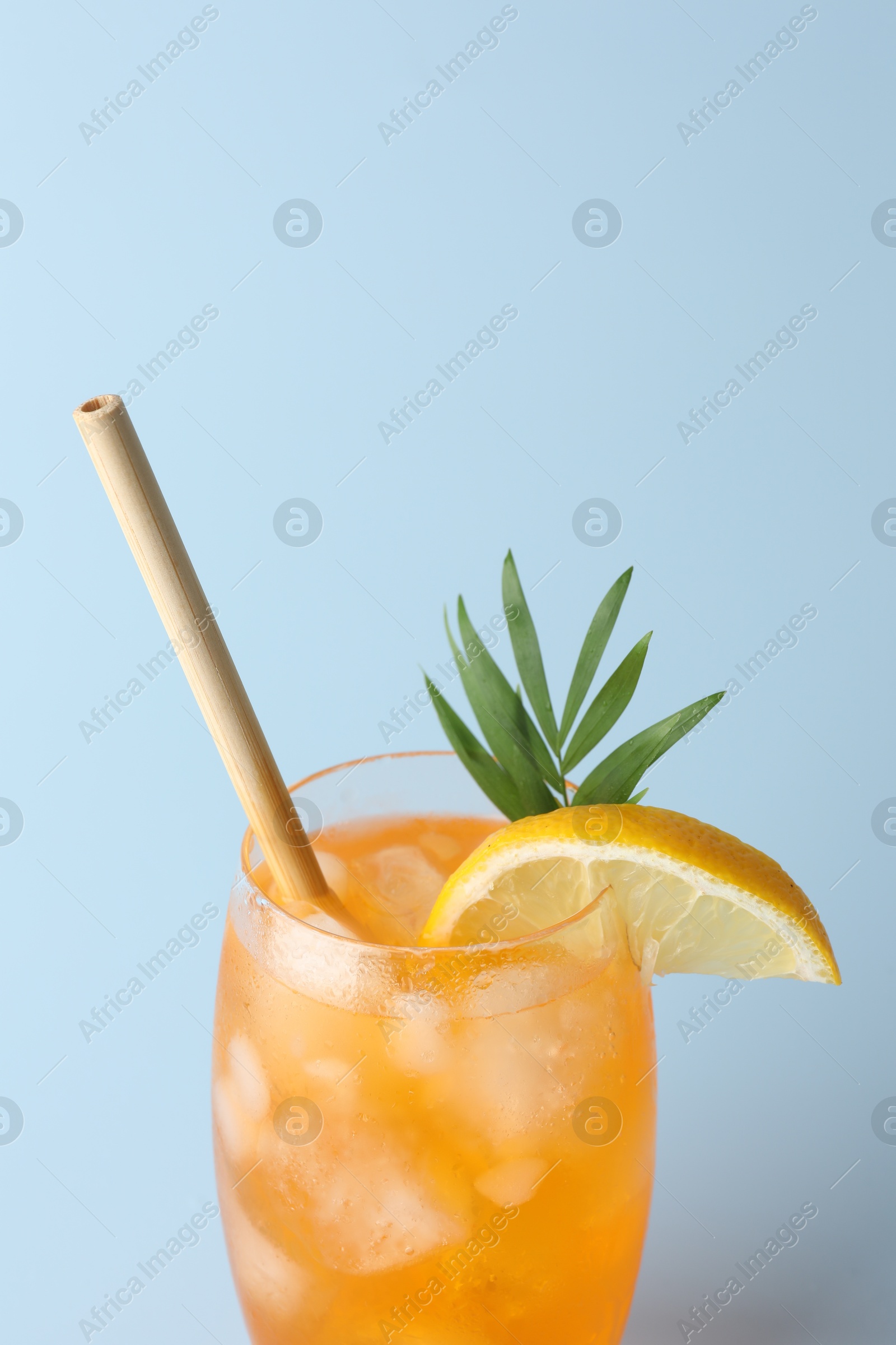 Photo of Tasty refreshing drink with straw in glass on light blue background, closeup