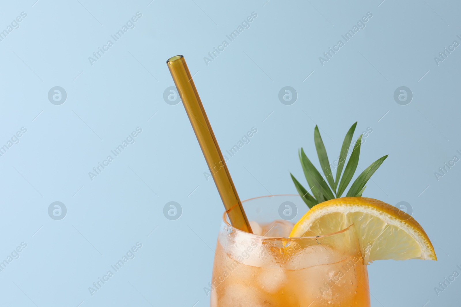 Photo of Tasty refreshing drink with straw in glass on light blue background, closeup