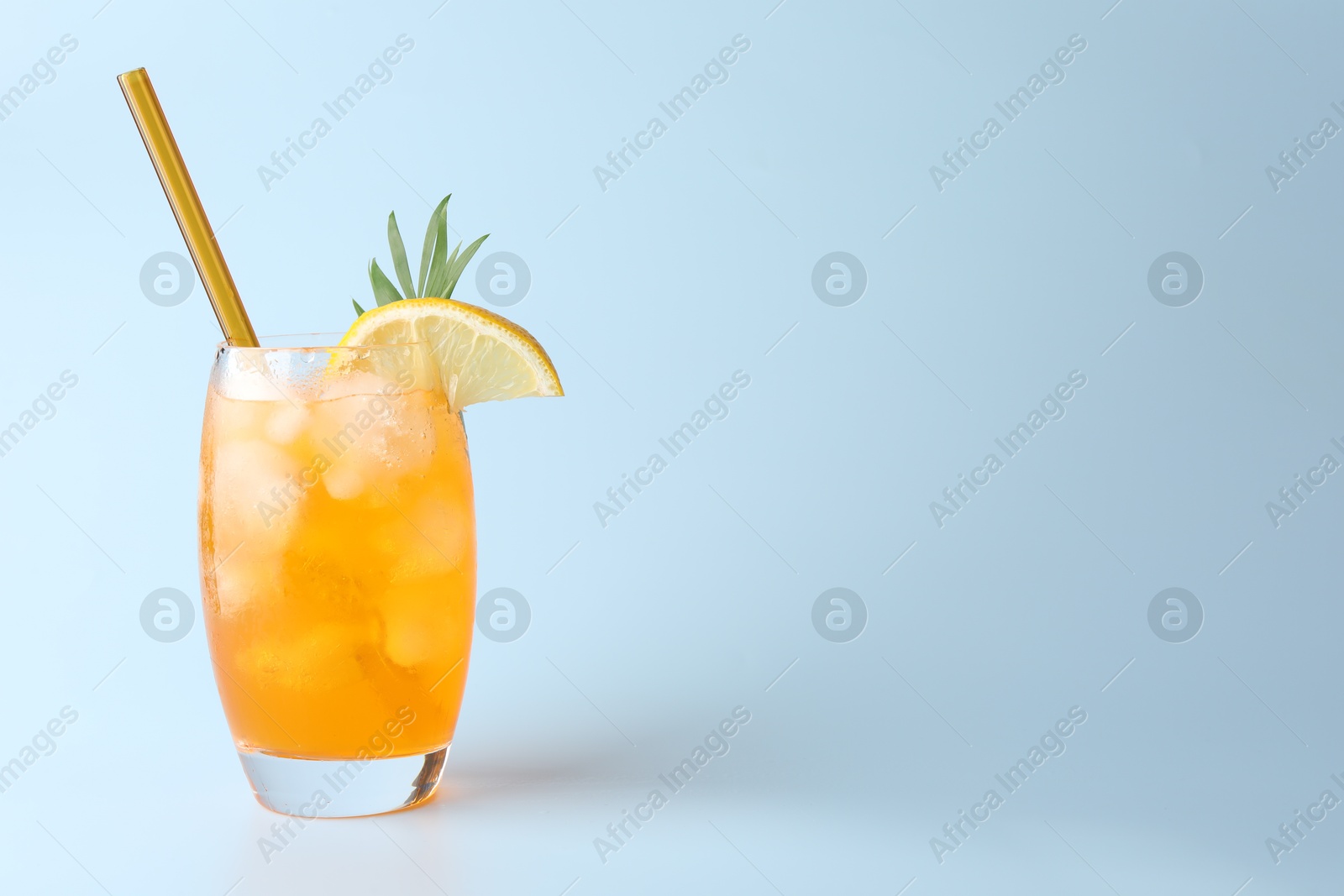 Photo of Tasty refreshing drink with straw in glass on light blue background, space for text