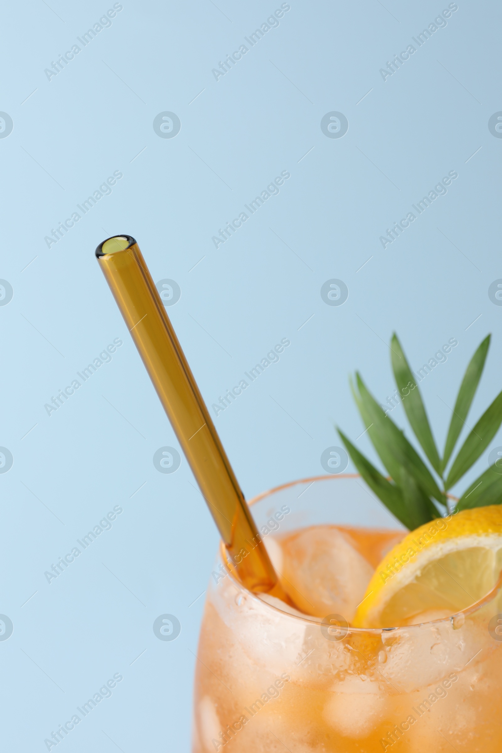 Photo of Tasty refreshing drink with straw in glass on light blue background, closeup