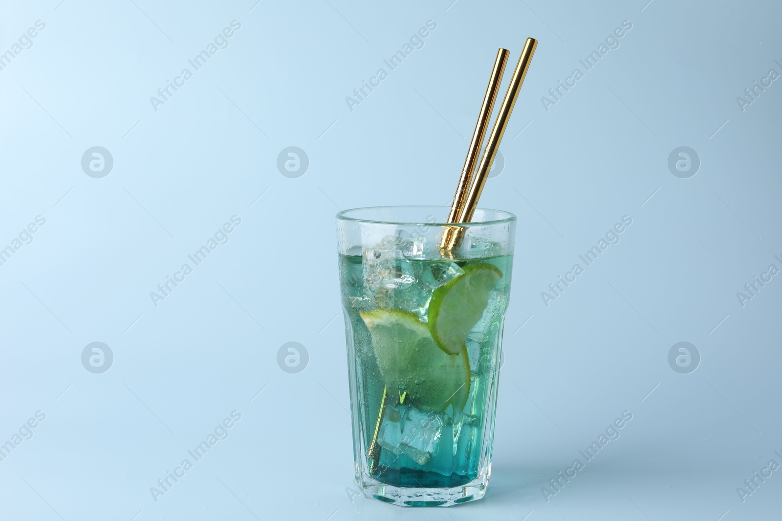 Photo of Tasty refreshing drink with straws in glass on light blue background