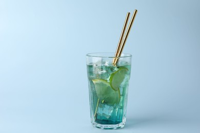 Tasty refreshing drink with straws in glass on light blue background