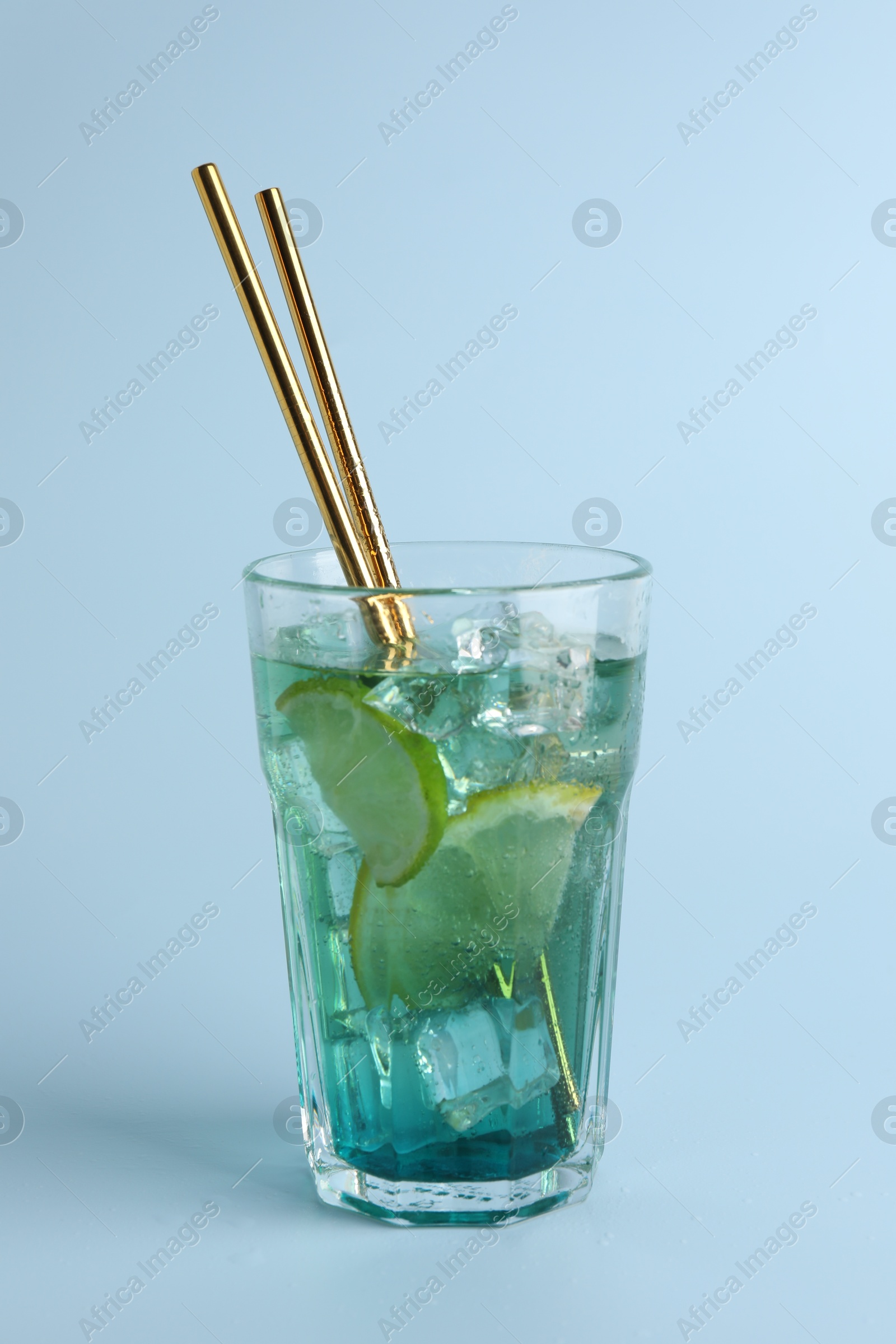 Photo of Tasty refreshing drink with straws in glass on light blue background