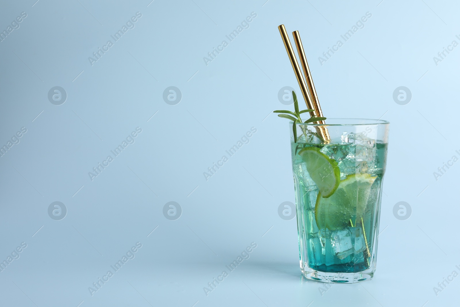 Photo of Tasty refreshing drink with straws in glass on light blue background, space for text