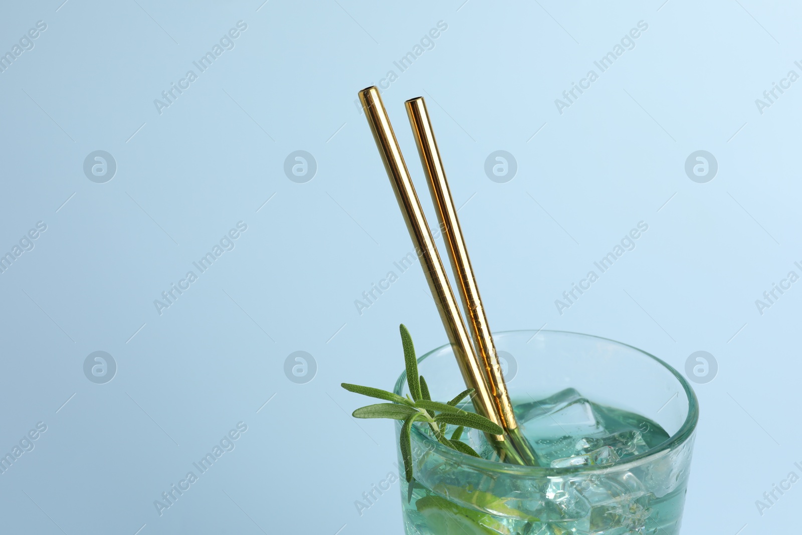 Photo of Tasty refreshing drink with straws in glass on light blue background, closeup. Space for text