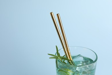 Tasty refreshing drink with straws in glass on light blue background, closeup. Space for text