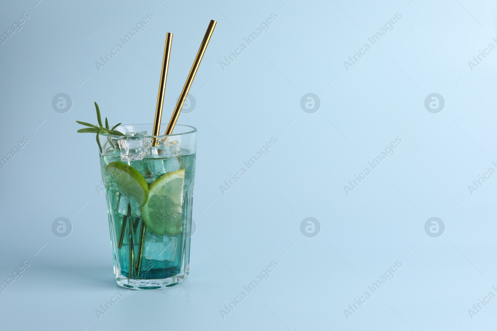 Photo of Tasty refreshing drink with straws in glass on light blue background, space for text