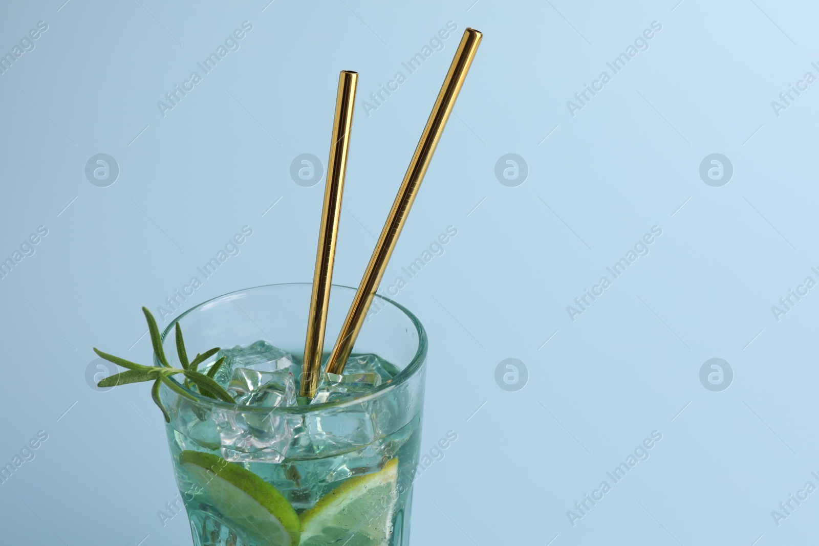 Photo of Tasty refreshing drink with straws in glass on light blue background, closeup. Space for text