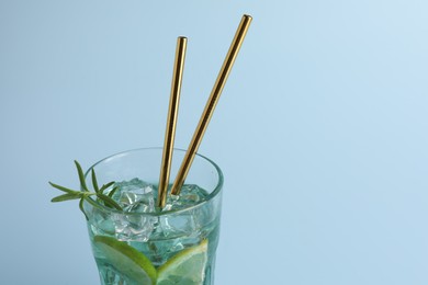 Photo of Tasty refreshing drink with straws in glass on light blue background, closeup. Space for text