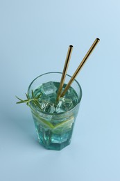 Tasty refreshing drink with straws in glass on light blue background