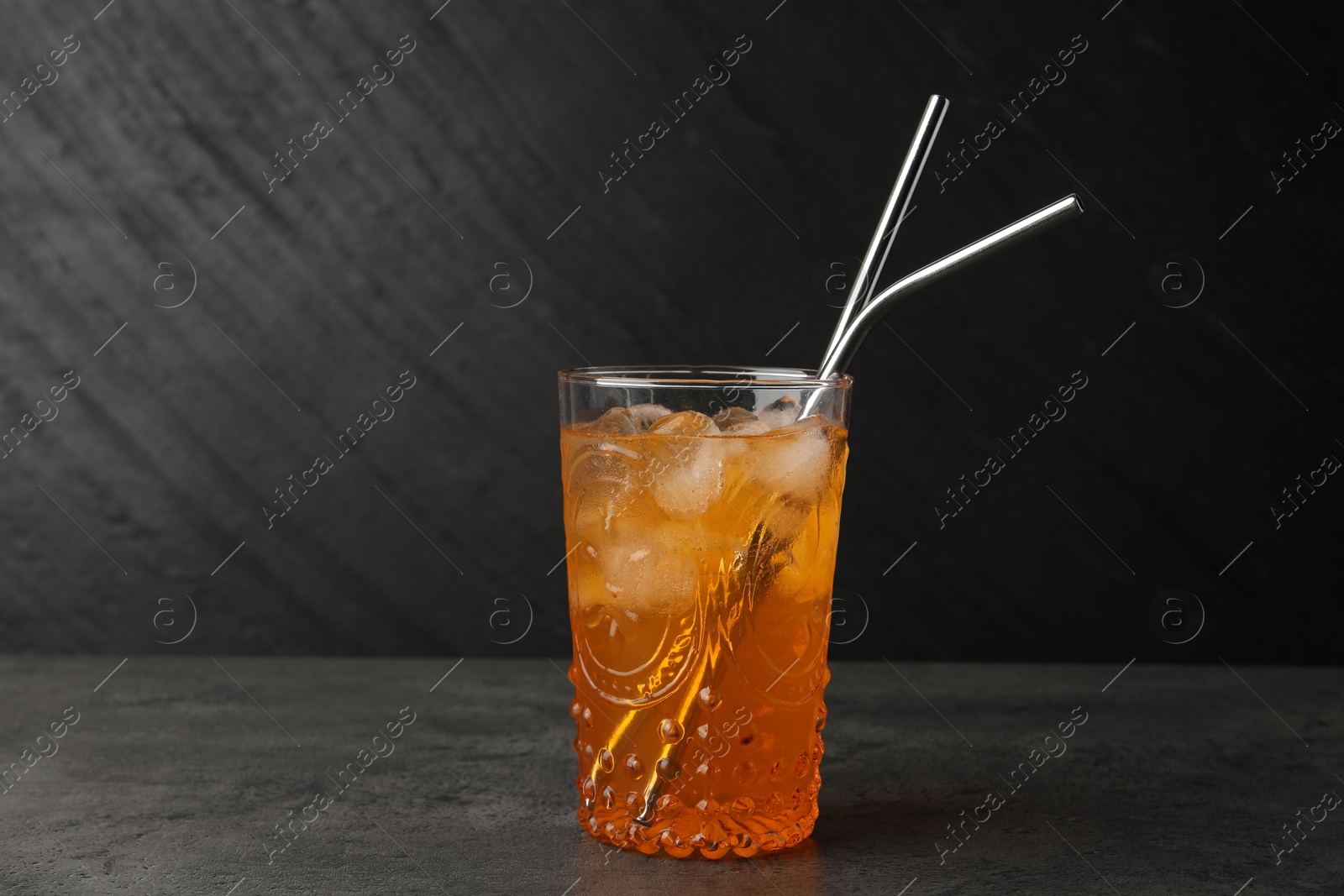 Photo of Tasty refreshing drink with straws in glass on grey textured table