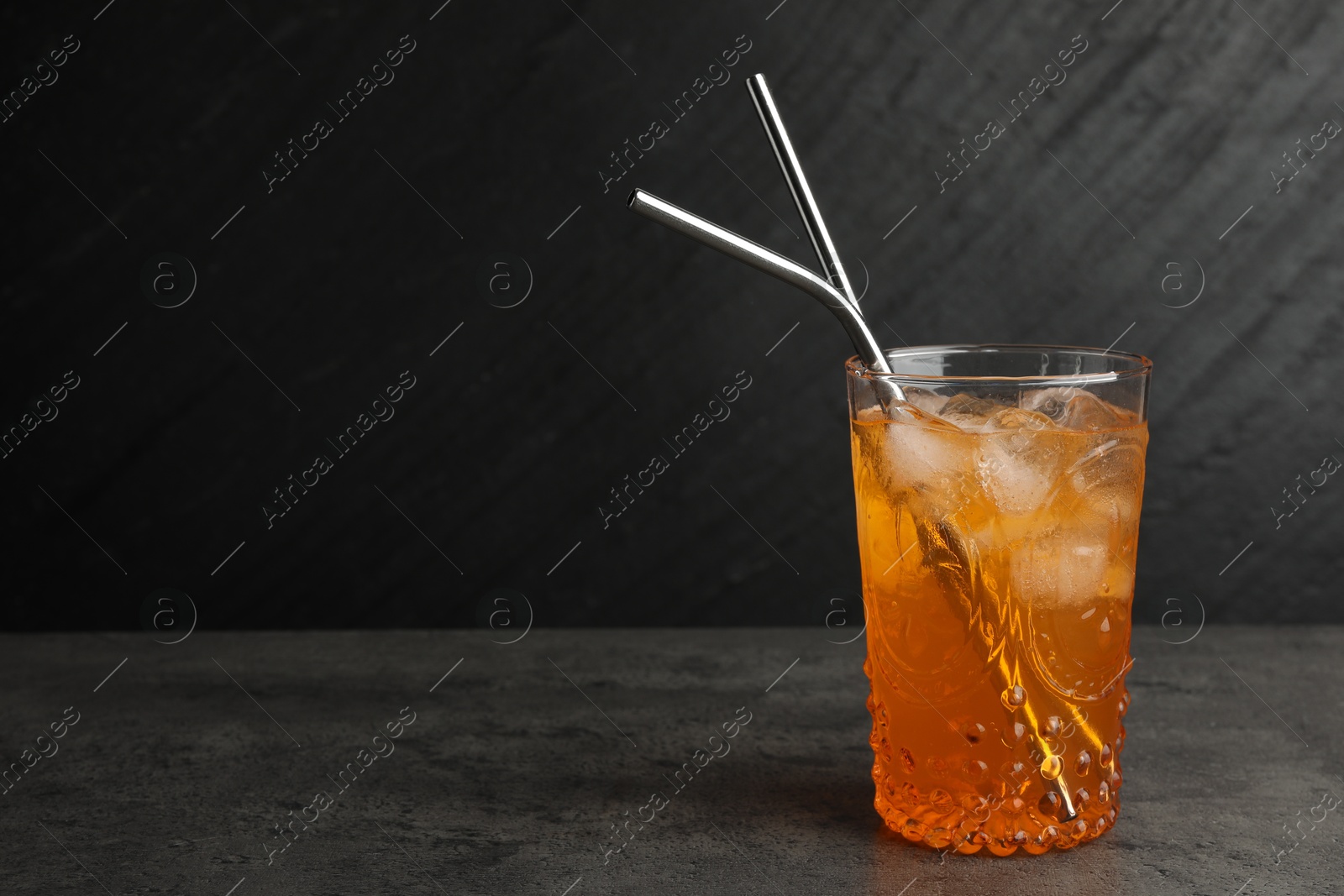 Photo of Tasty refreshing drink with straws in glass on grey textured table, space for text