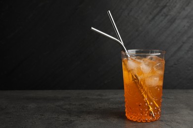 Photo of Tasty refreshing drink with straws in glass on grey textured table, space for text